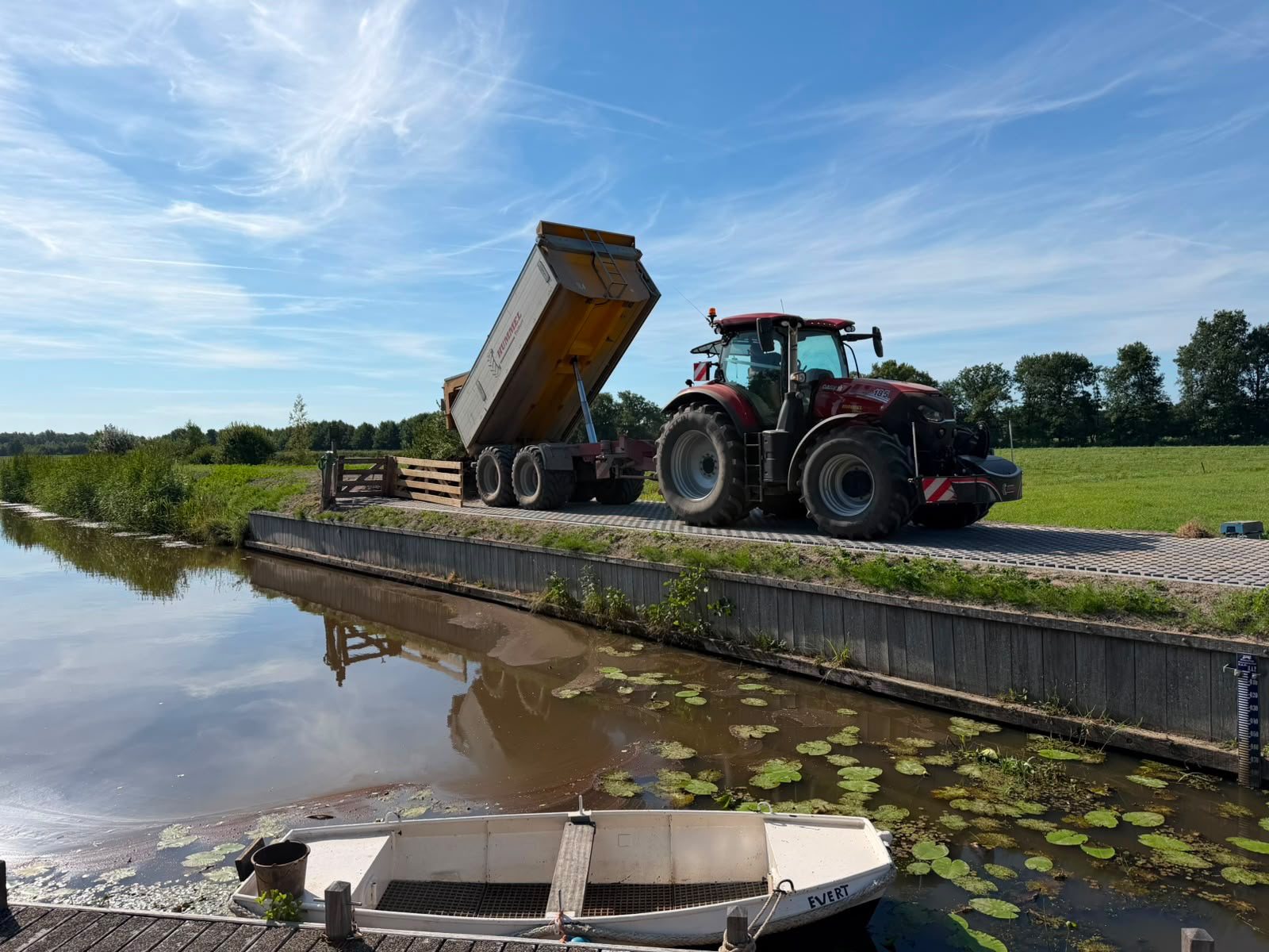 Tractor met kipper lost grond langs de vaart