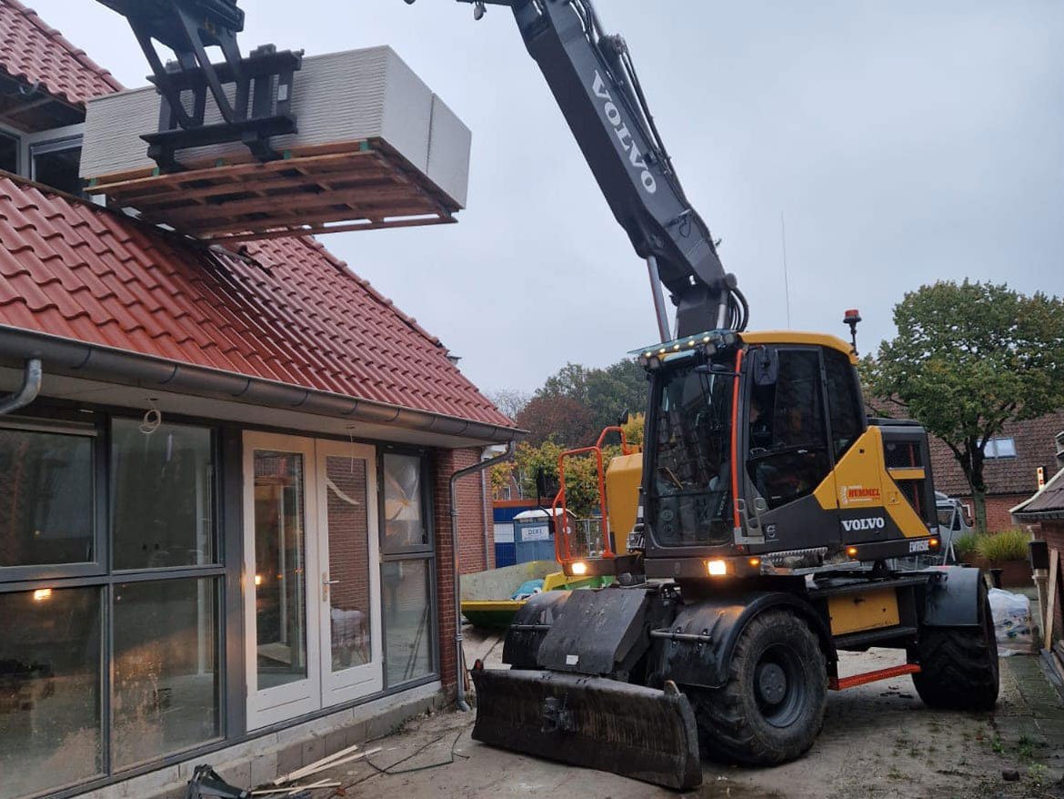 Kraan hijst een pallet stenen langs een woning