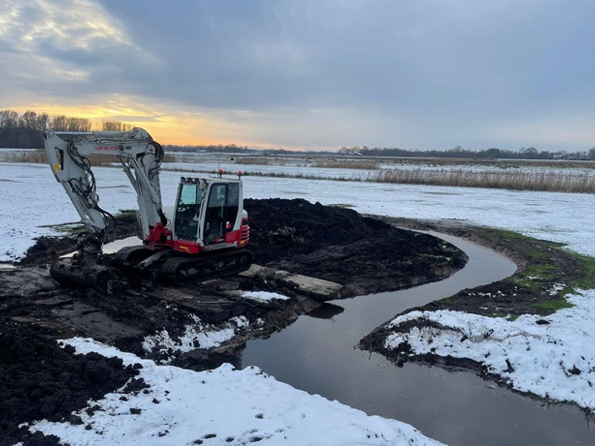 Takeuchi rupskraan graaft een watergang in de sneeuw