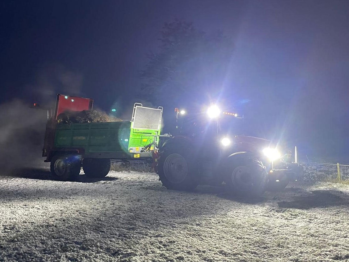 Tractor met meststrooier in het donker, met de werklampen aan