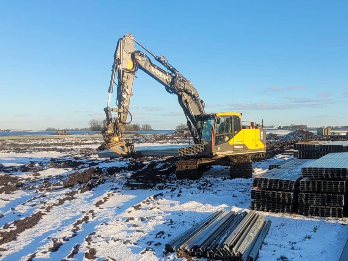 Rupskraan in een besneeuwd veld naast stapels drainagebuizen