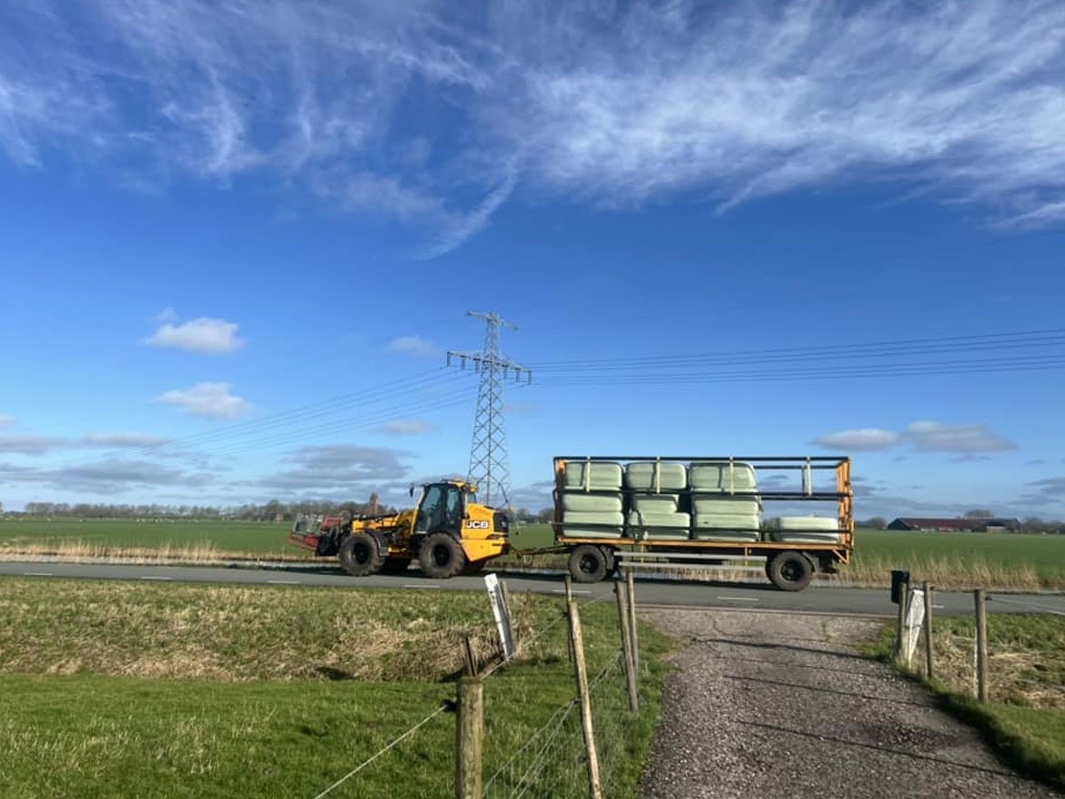 Shovel trekt een platte wagen met gewikkelde balen over een landweg