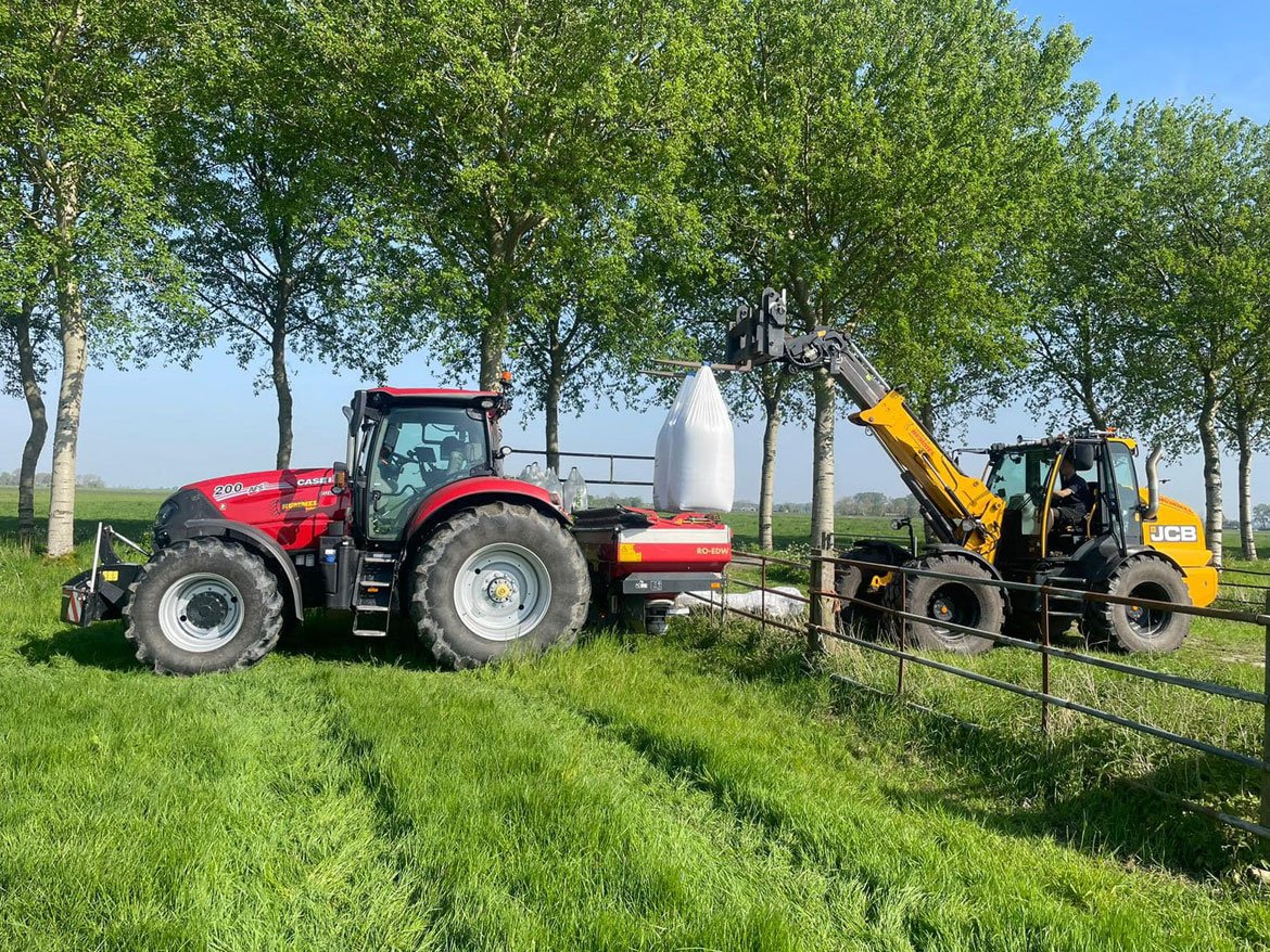 Shovel vult de kunstmeststrooier achter de tractor met een big bag