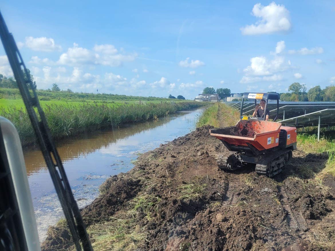 Rupsdumper rijdt grond langs een sloot, gezien vanuit de kraan