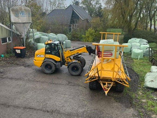 Shovel met balenwagen tussen de gewikkelde kuilbalen